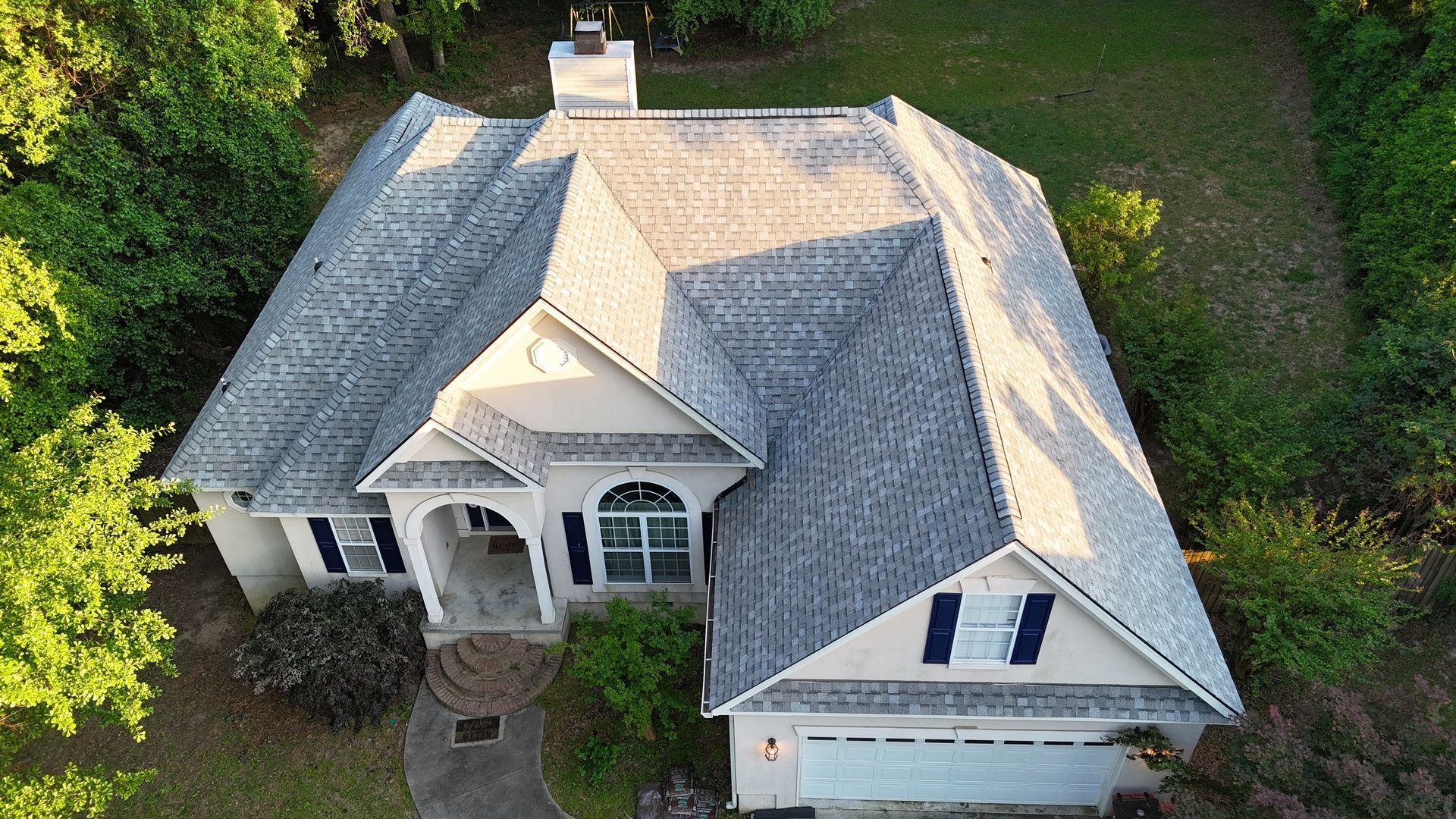 An aerial view of a large white house with a new gray roof surrounded by trees.