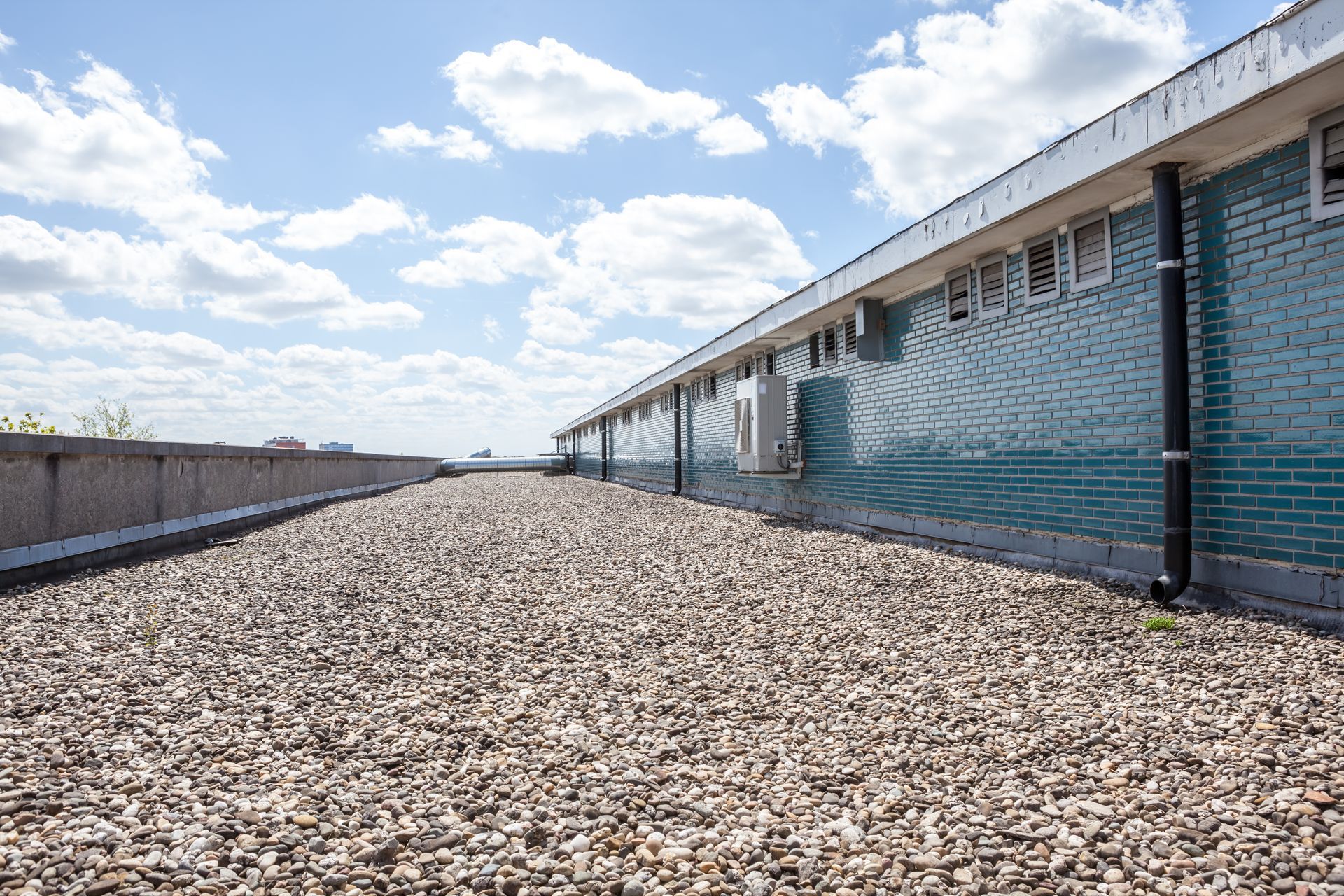 A gravel road leading to a brick building with a blue sky in the background.