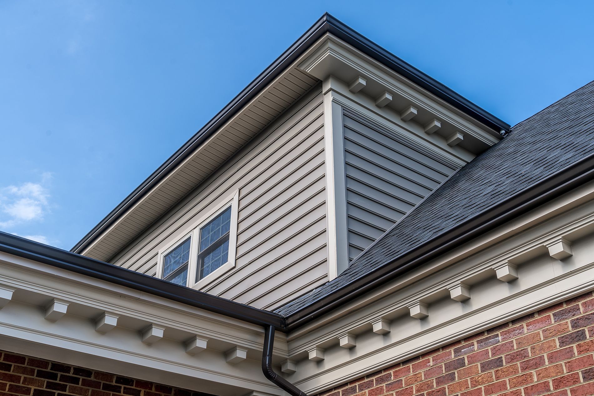 The roof of a brick house with a gray roof and white siding.
