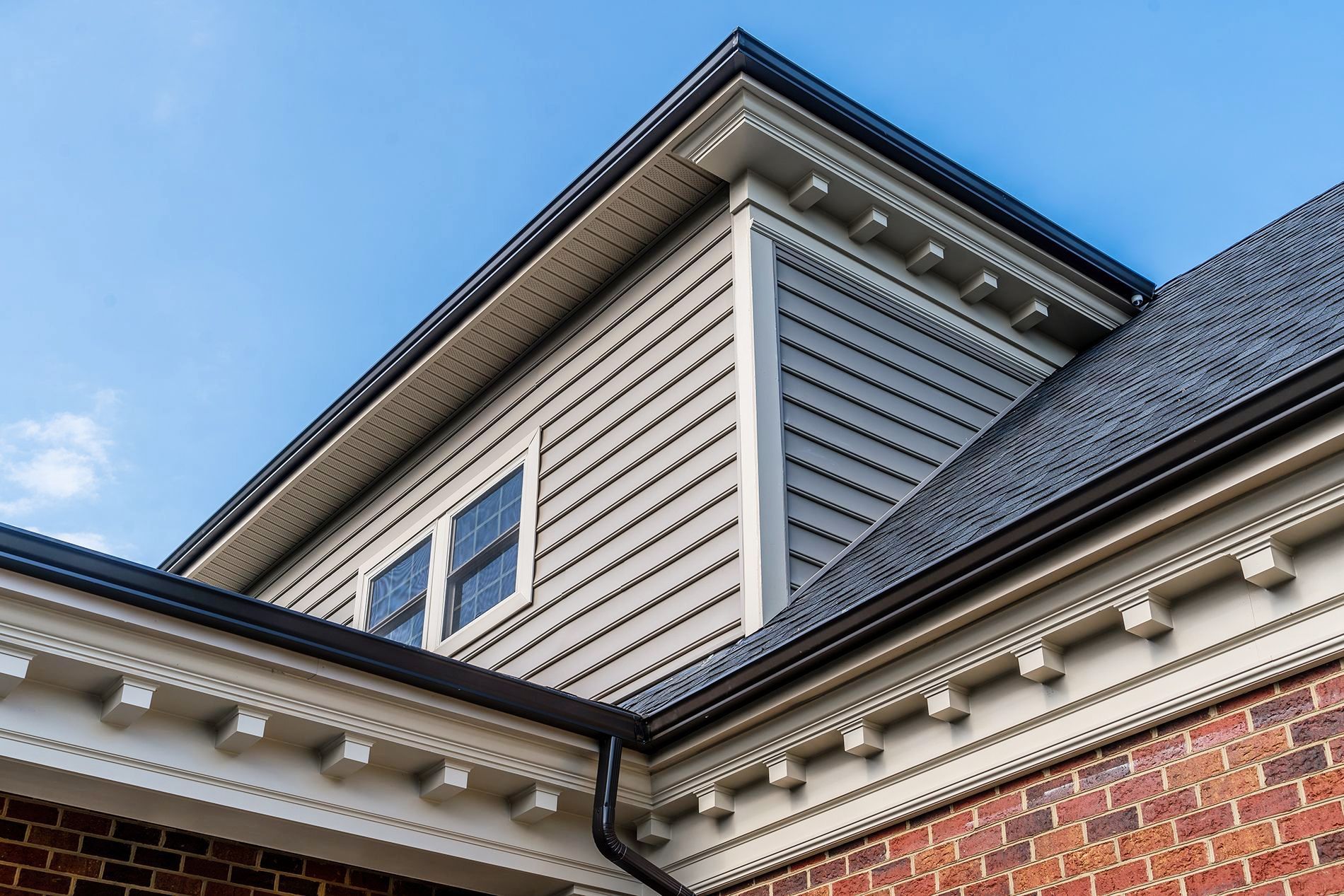 The roof of a brick house with a gray roof and a white siding.