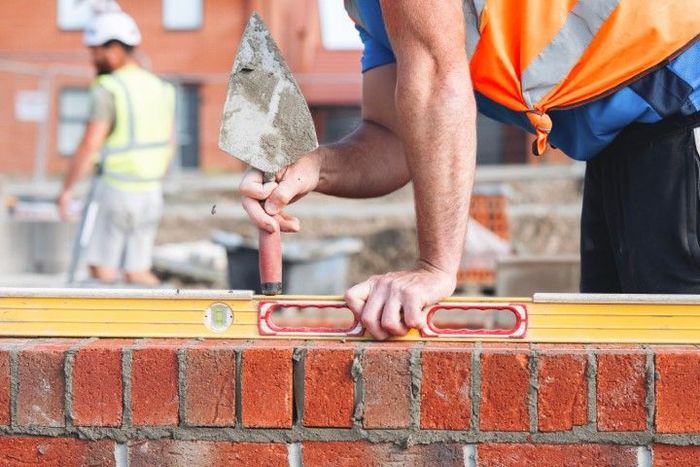 Bricklayer using a level to check brick alignment on a construction site.