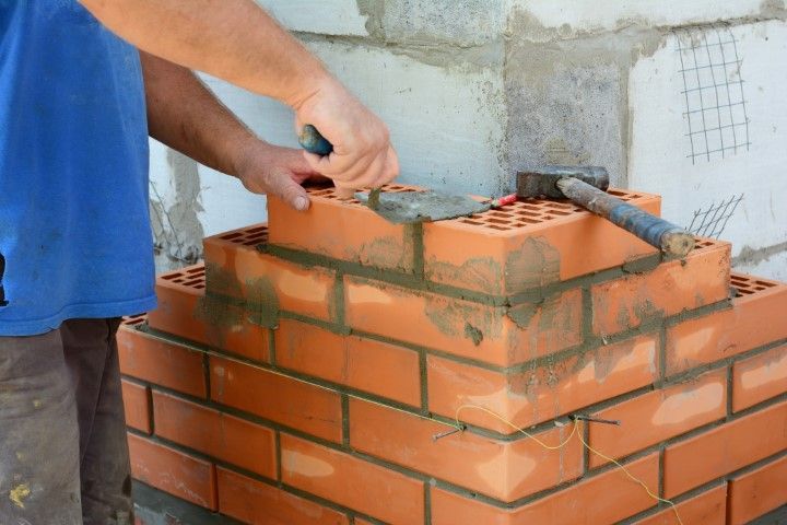 Person laying bricks, using a trowel to apply mortar. Corner of brick structure being built.