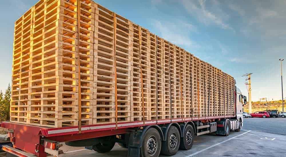 A truck filled with lots of wooden pallets is parked in a parking lot.