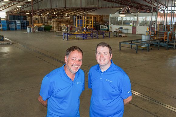 Two men in blue shirts are standing in a large warehouse.