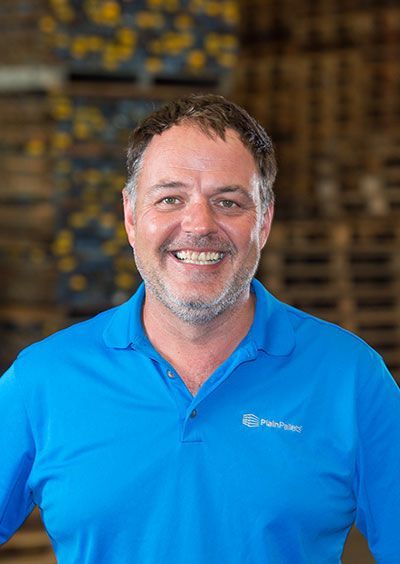 A man in a blue shirt is smiling for the camera in a warehouse.