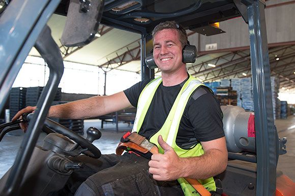 A man is driving a forklift in a warehouse and giving a thumbs up.