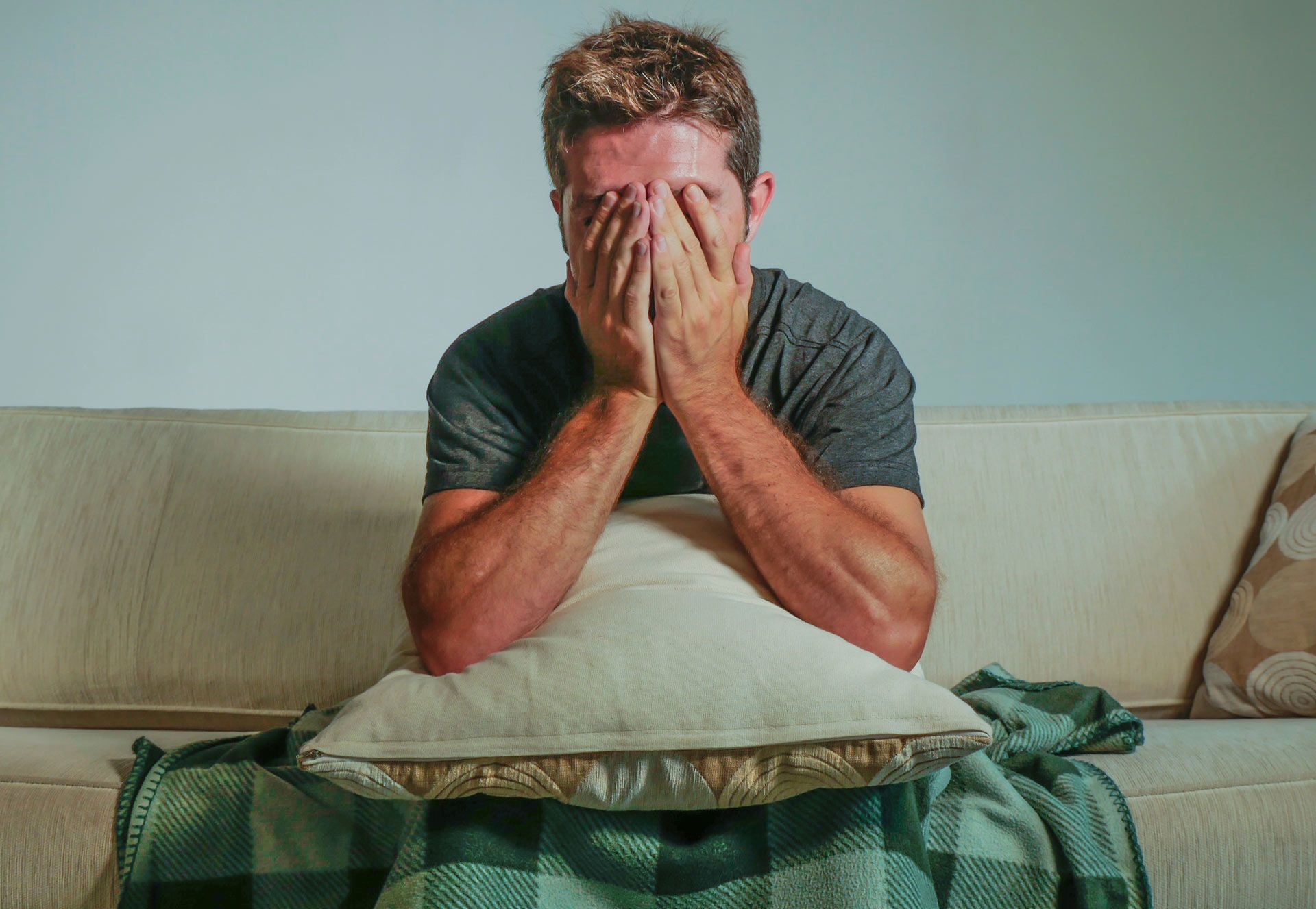 Man sitting on a sofa with hands covering face; appears distressed.