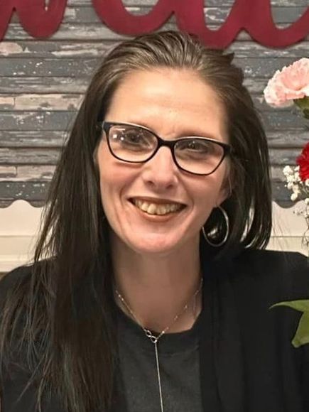 A woman wearing glasses and earrings is smiling for the camera.