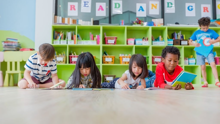 A group of children are laying on the floor reading books in a classroom.