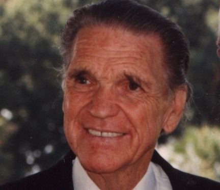 An older man in a suit and tie smiles for the camera