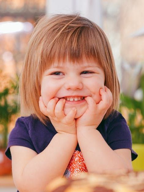 A little girl is smiling with her hands on her face.