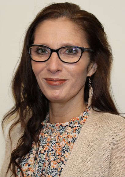 A woman wearing glasses and earrings is smiling for the camera.