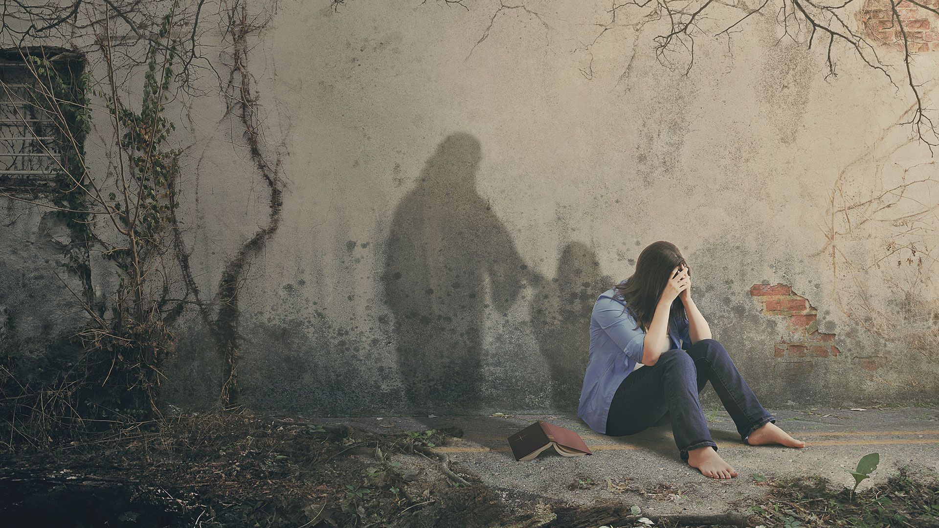 Woman with head in hands sits by a wall; a dark shadow extends a hand toward her.