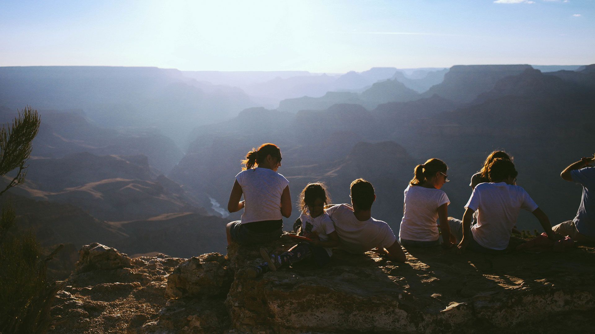 People overlooking the Grand Canyon at sunset. Mountains and hazy landscape in the background.