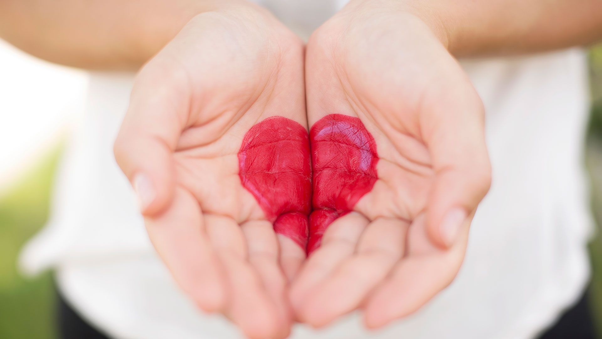 Hands cupped, holding a red, heart-shaped smear. Soft focus, outdoors, daylight.
