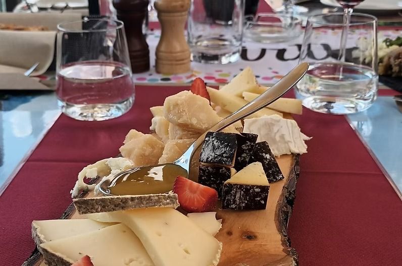 Tagliere con vari formaggi, fragole e un cucchiaio su un vassoio di legno al tavolo.