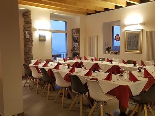 Sala da pranzo del ristorante con tavoli apparecchiati, tovaglioli rossi, sedie bianche e grigie, luci soffuse.