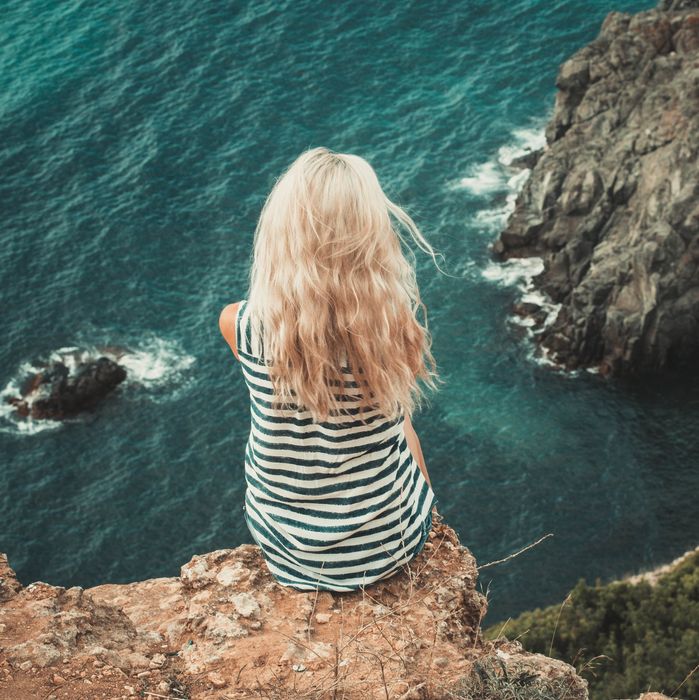 Woman in a striped tank top sitting on cliff overlooking the rocks and the ocean below her