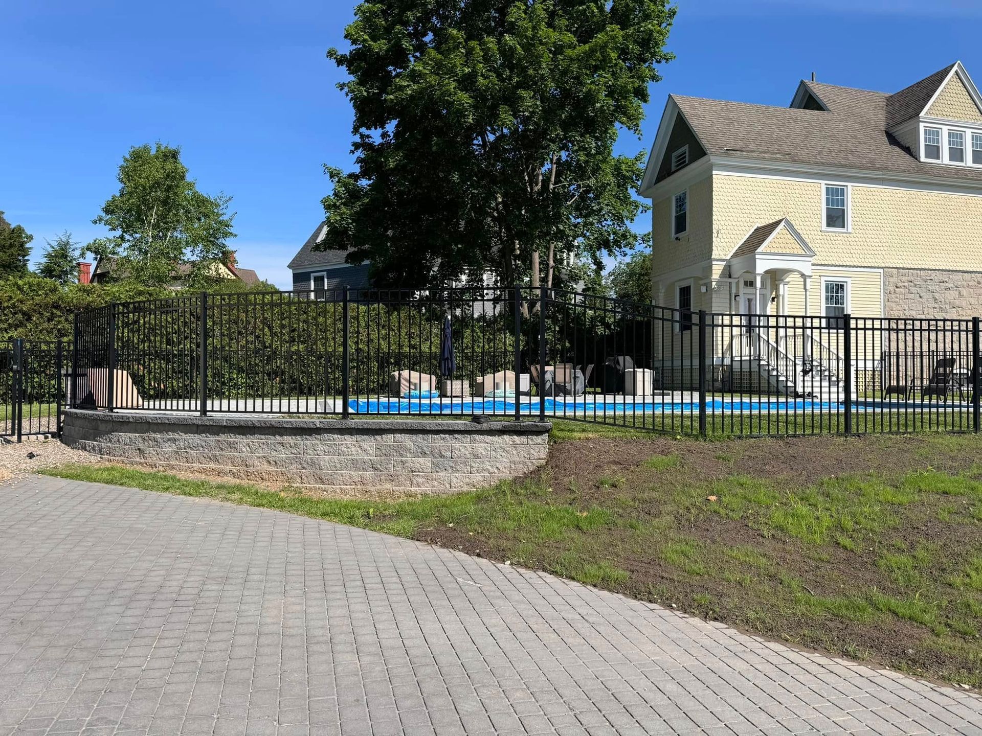 A fence surrounds a swimming pool in front of a house.