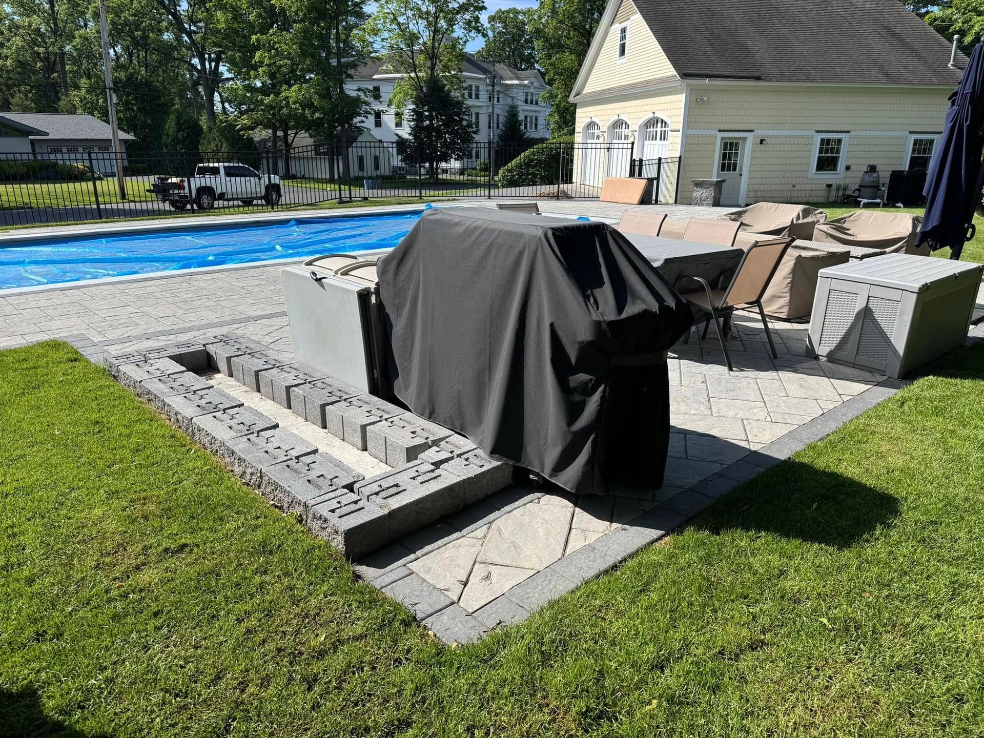 A grill is sitting in the grass next to a pool.