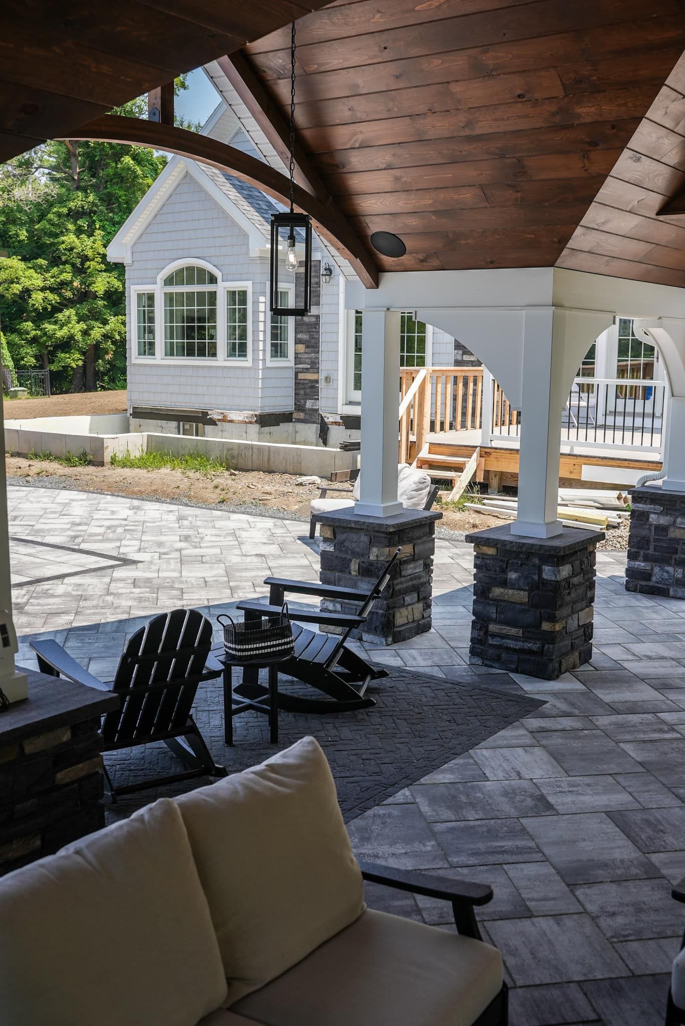 A patio with a couch and chairs under a wooden roof.