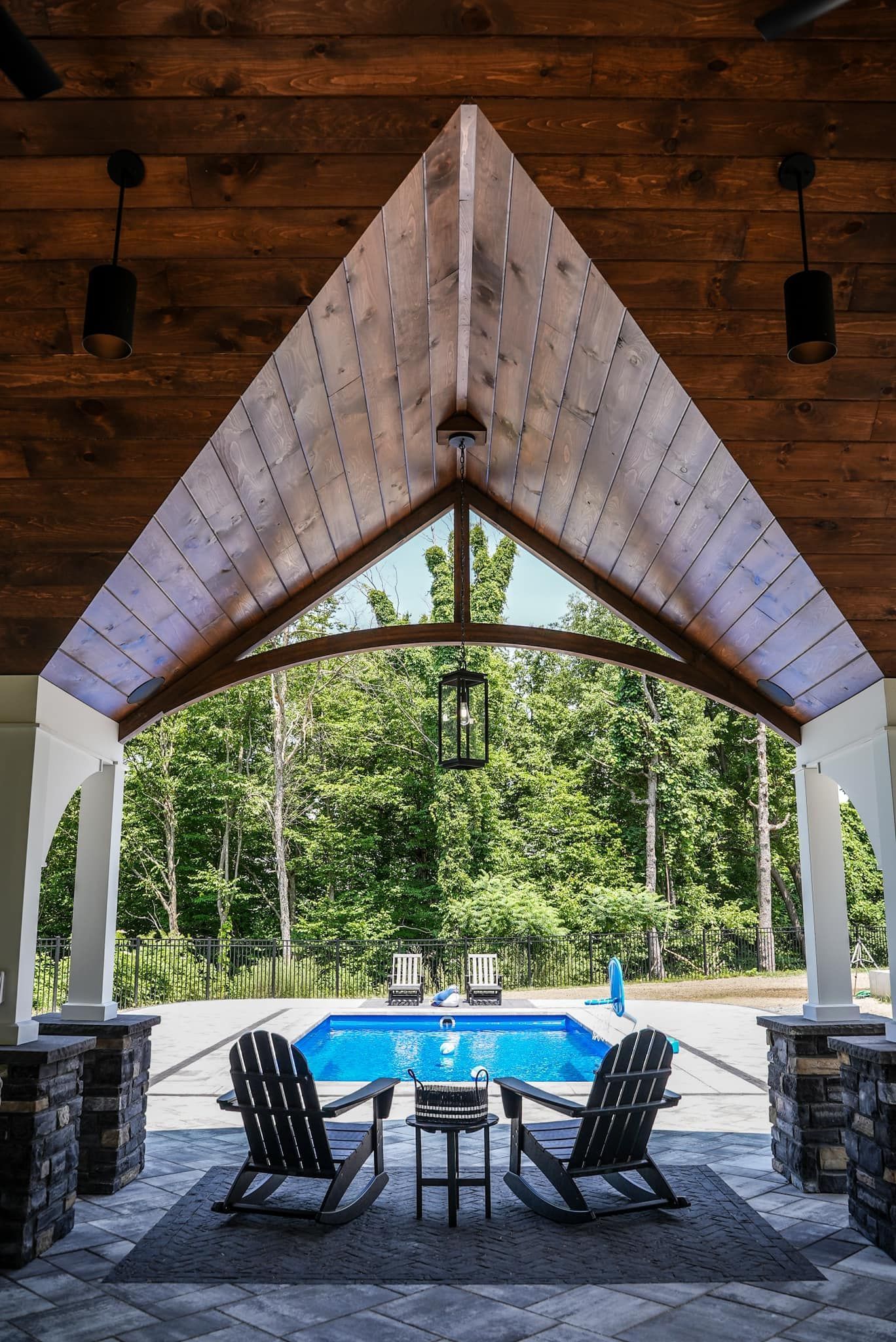 Two rocking chairs are sitting under a wooden roof next to a pool.