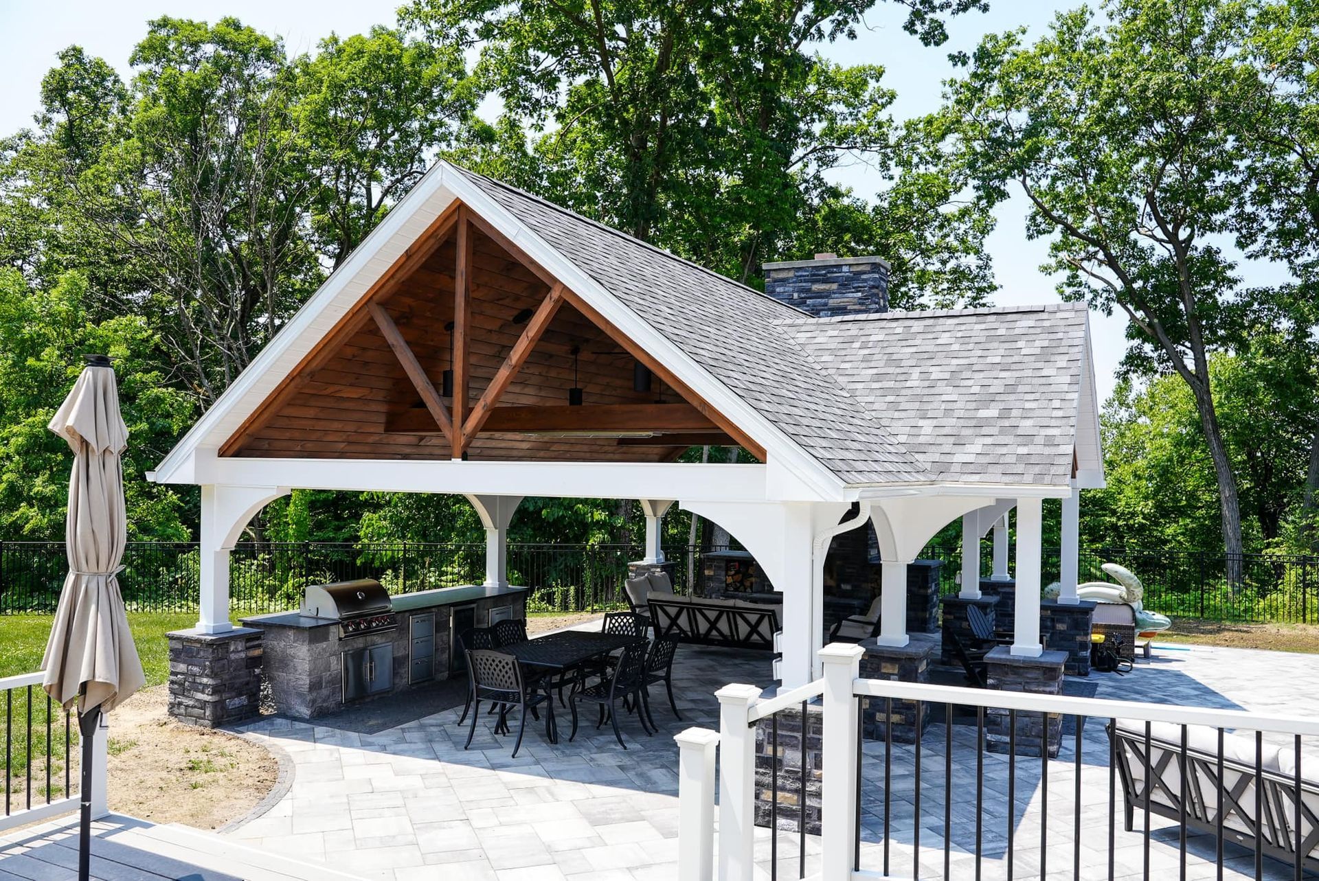 A large white pavilion with a wooden roof is surrounded by trees.