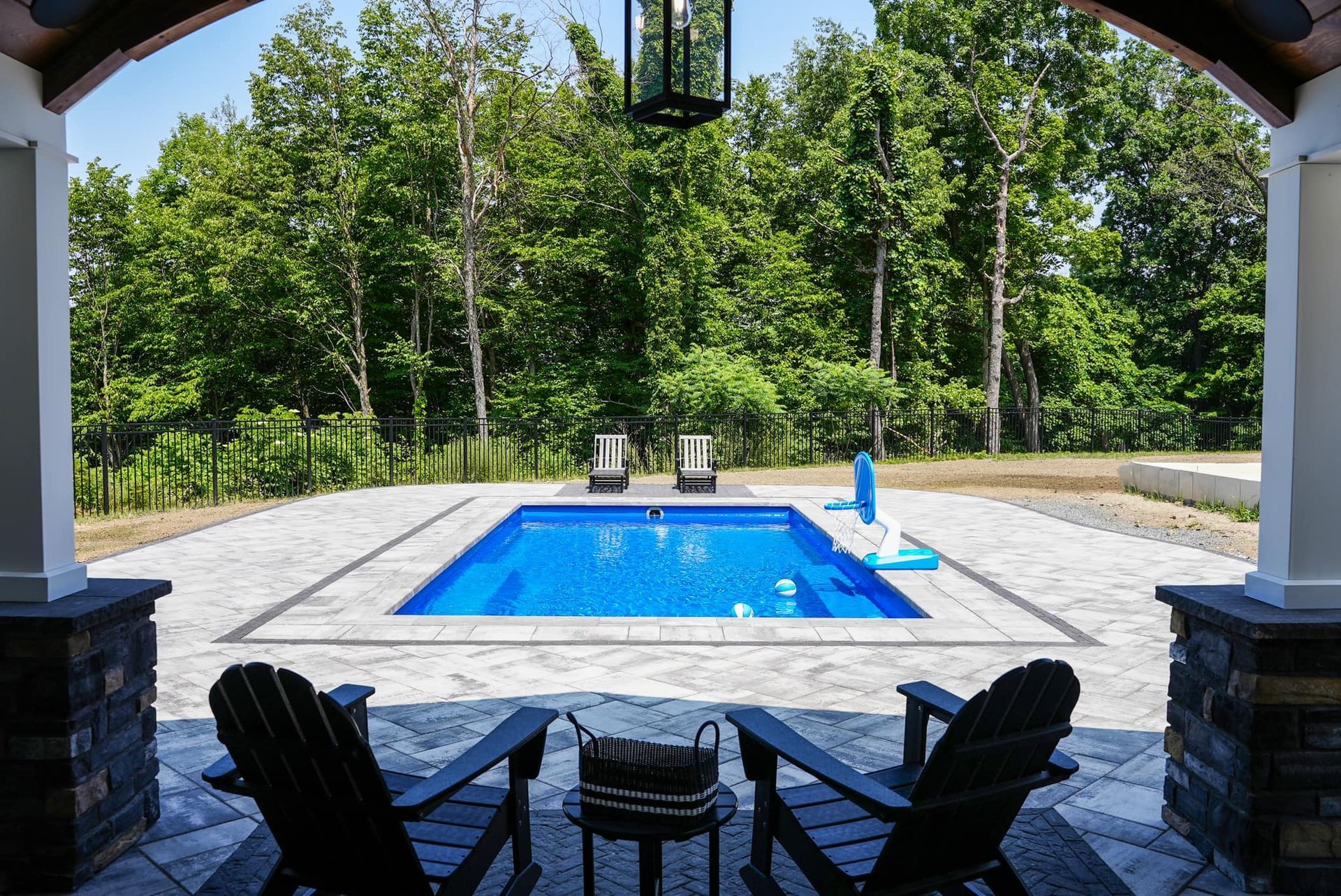 Two chairs are sitting in front of a large swimming pool surrounded by trees.