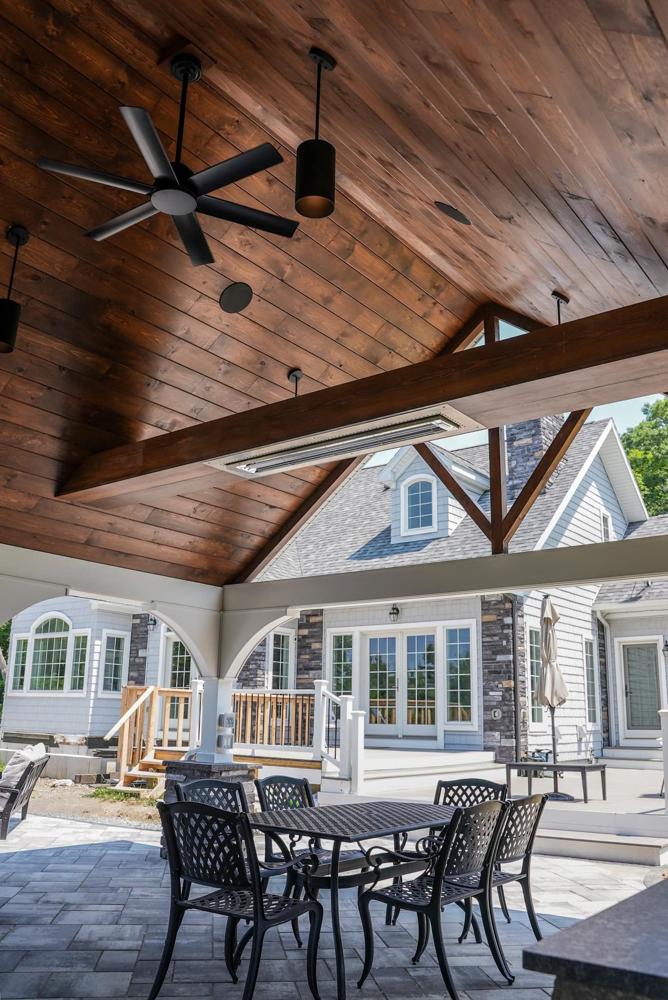 A patio with tables and chairs under a wooden ceiling with a ceiling fan.