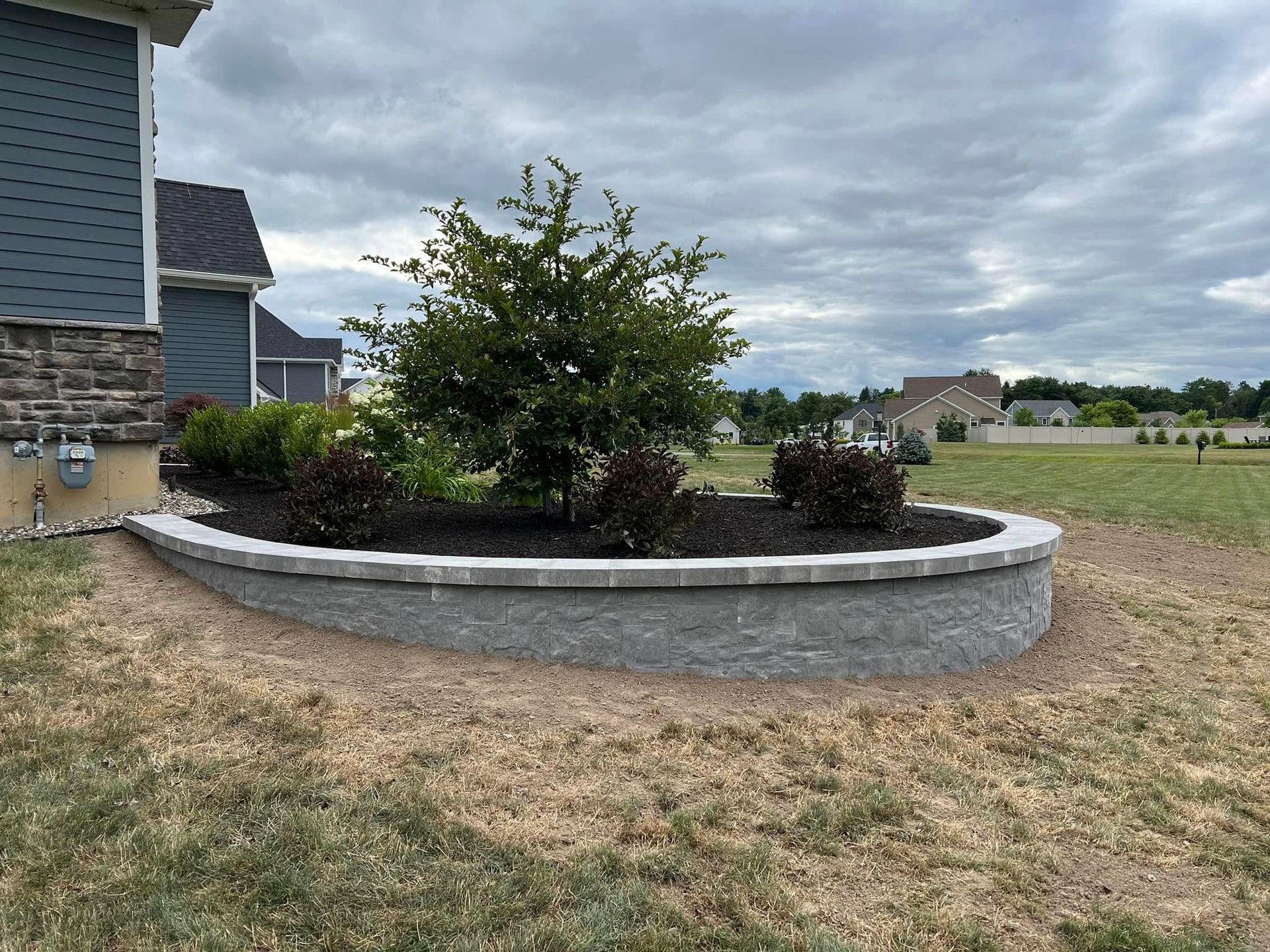 A circular planter with a tree in the middle of it in front of a house.