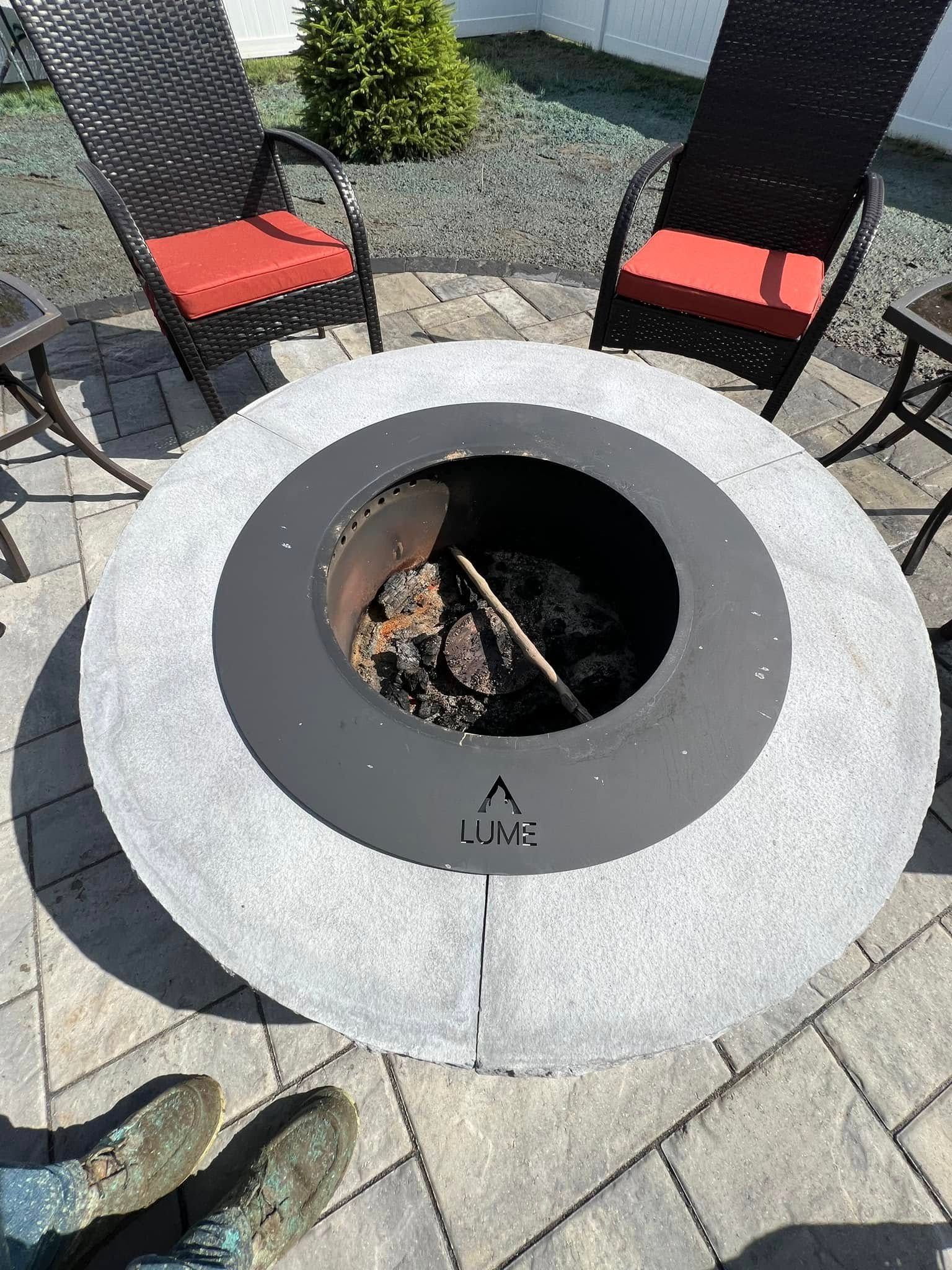 A fire pit is sitting on top of a patio next to wicker chairs.