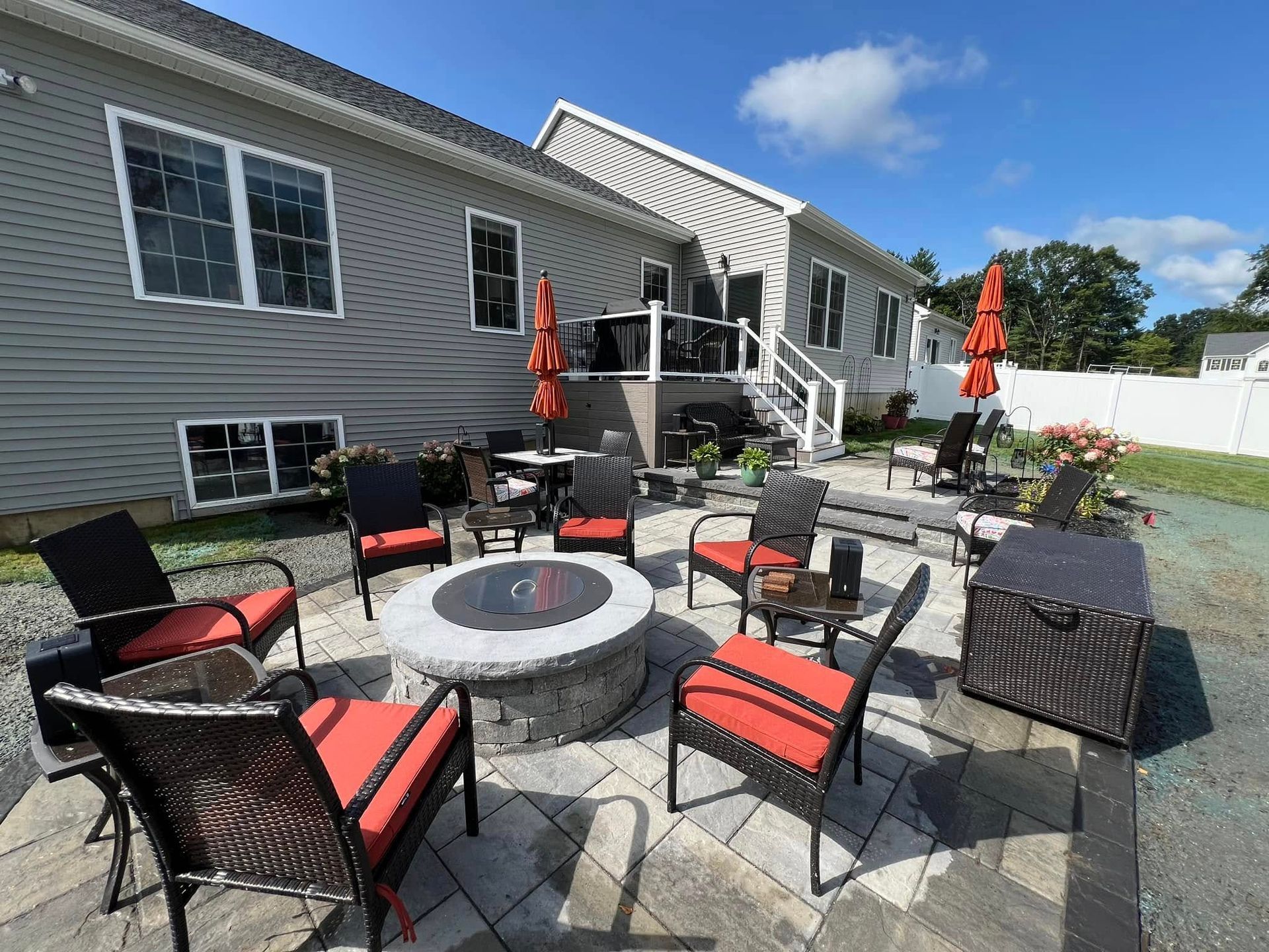 A patio with a fire pit and chairs in front of a house.