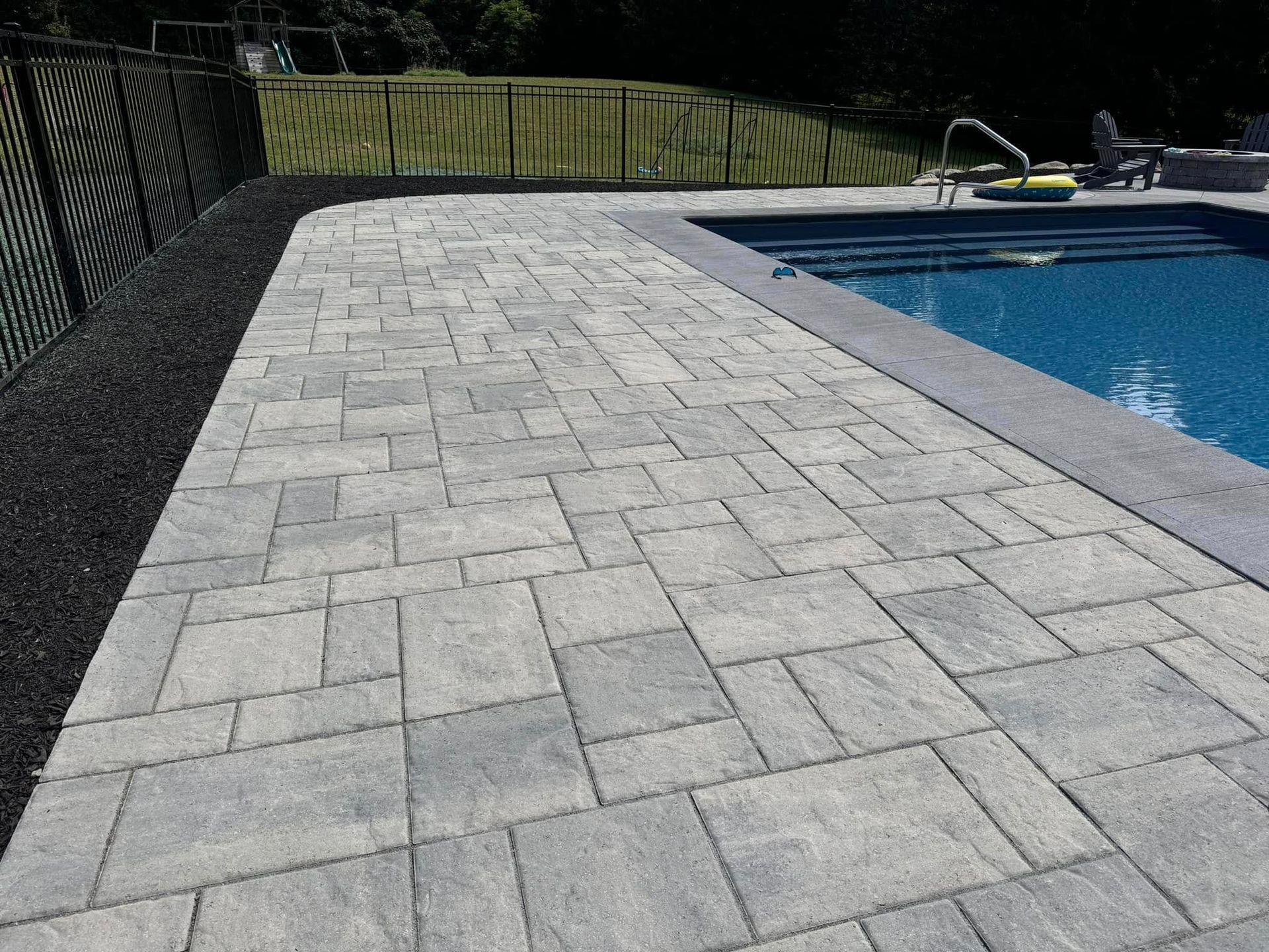 A patio next to a swimming pool with a fence in the background.