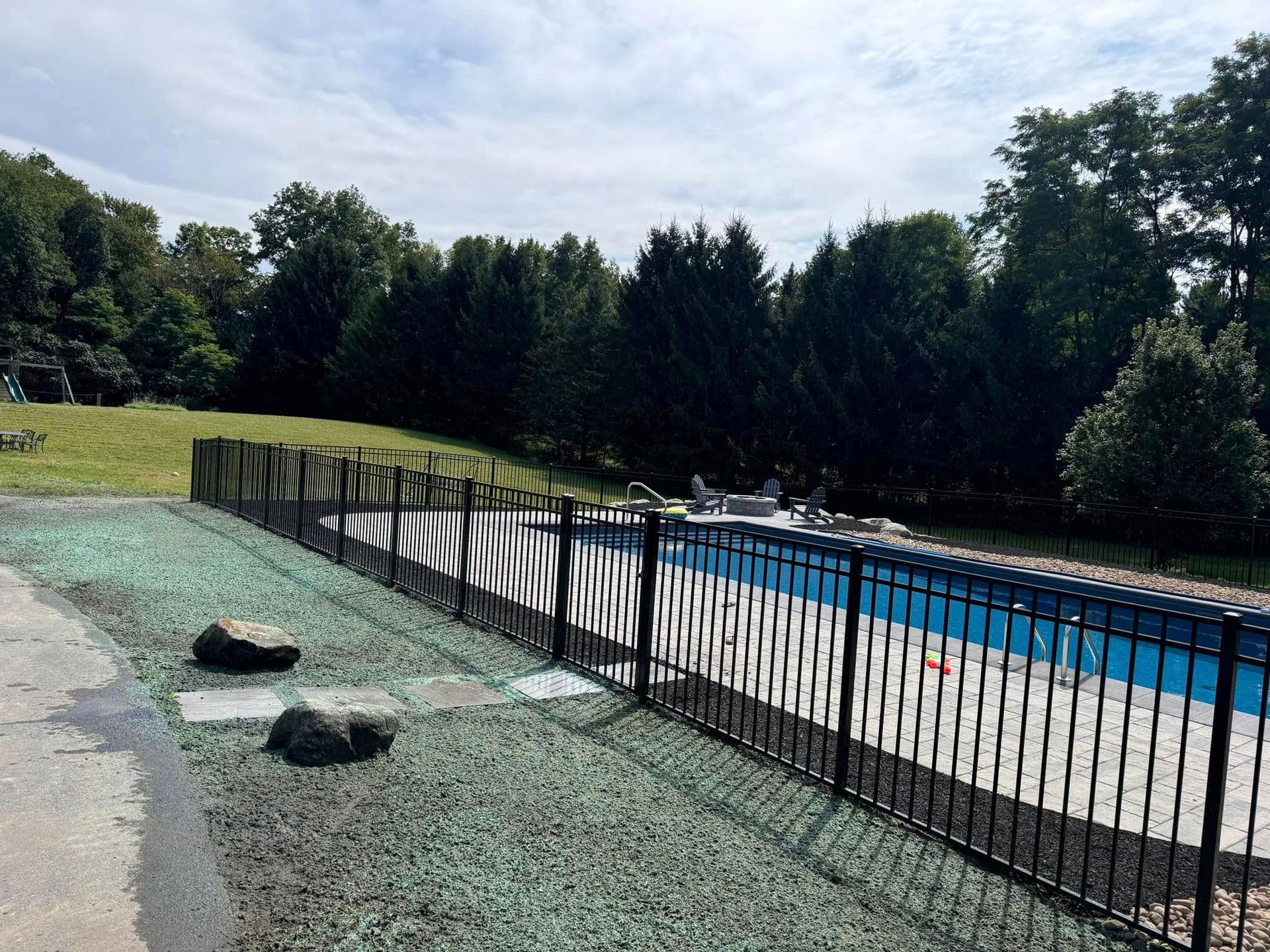 A fence surrounds a swimming pool with trees in the background