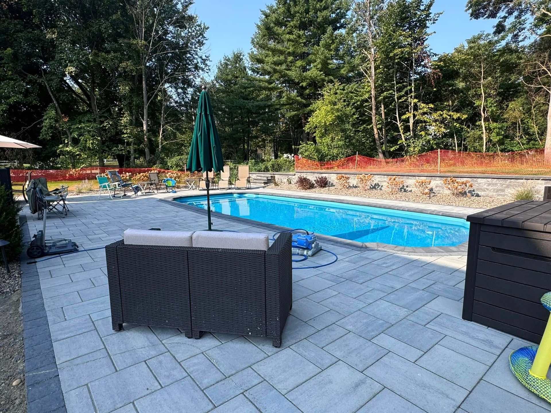 A patio with a couch and umbrella next to a large swimming pool.