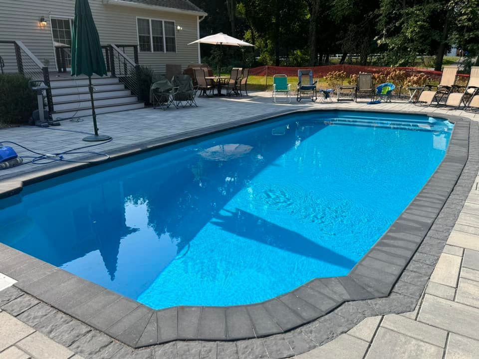 A large swimming pool is surrounded by chairs and umbrellas in a backyard.
