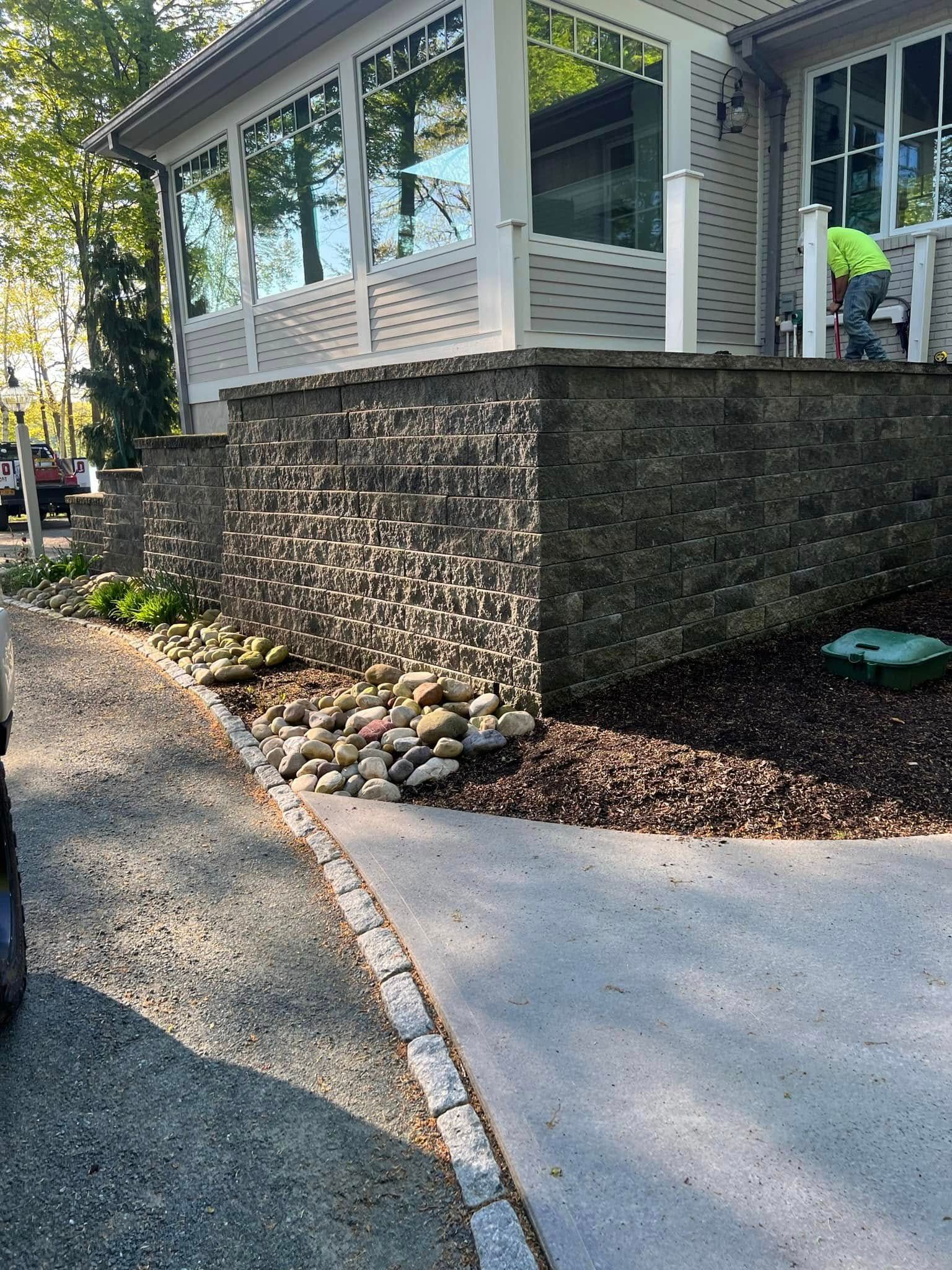 A car is parked in front of a house with a stone wall.