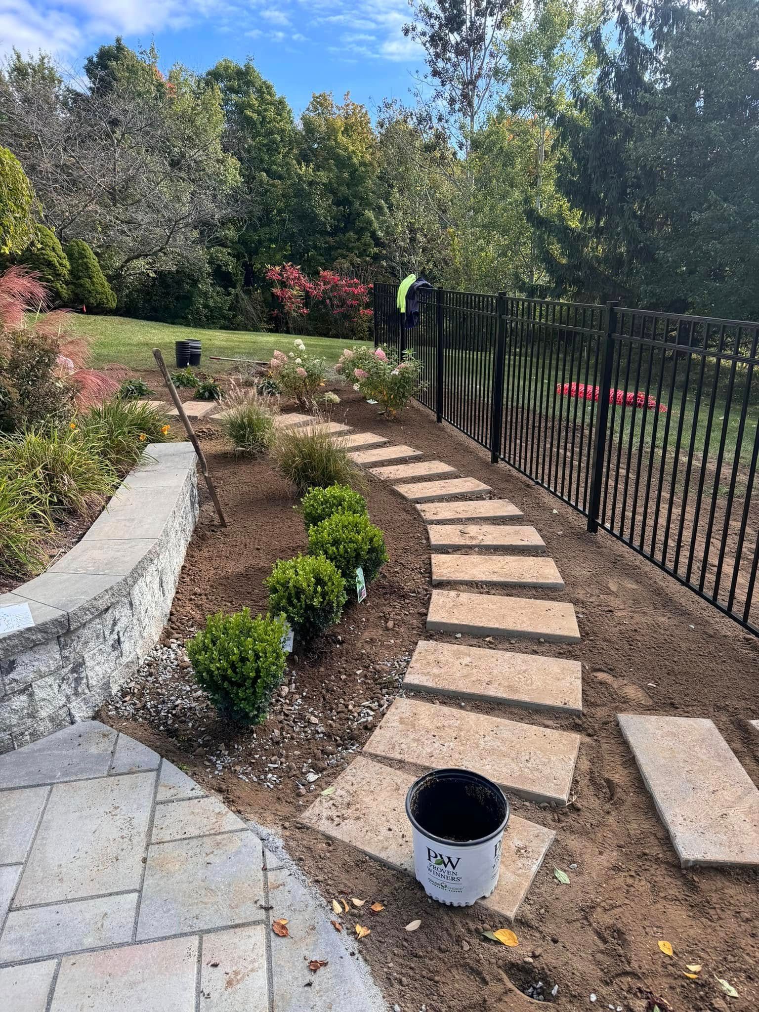 A stone walkway is being built in a backyard next to a fence.