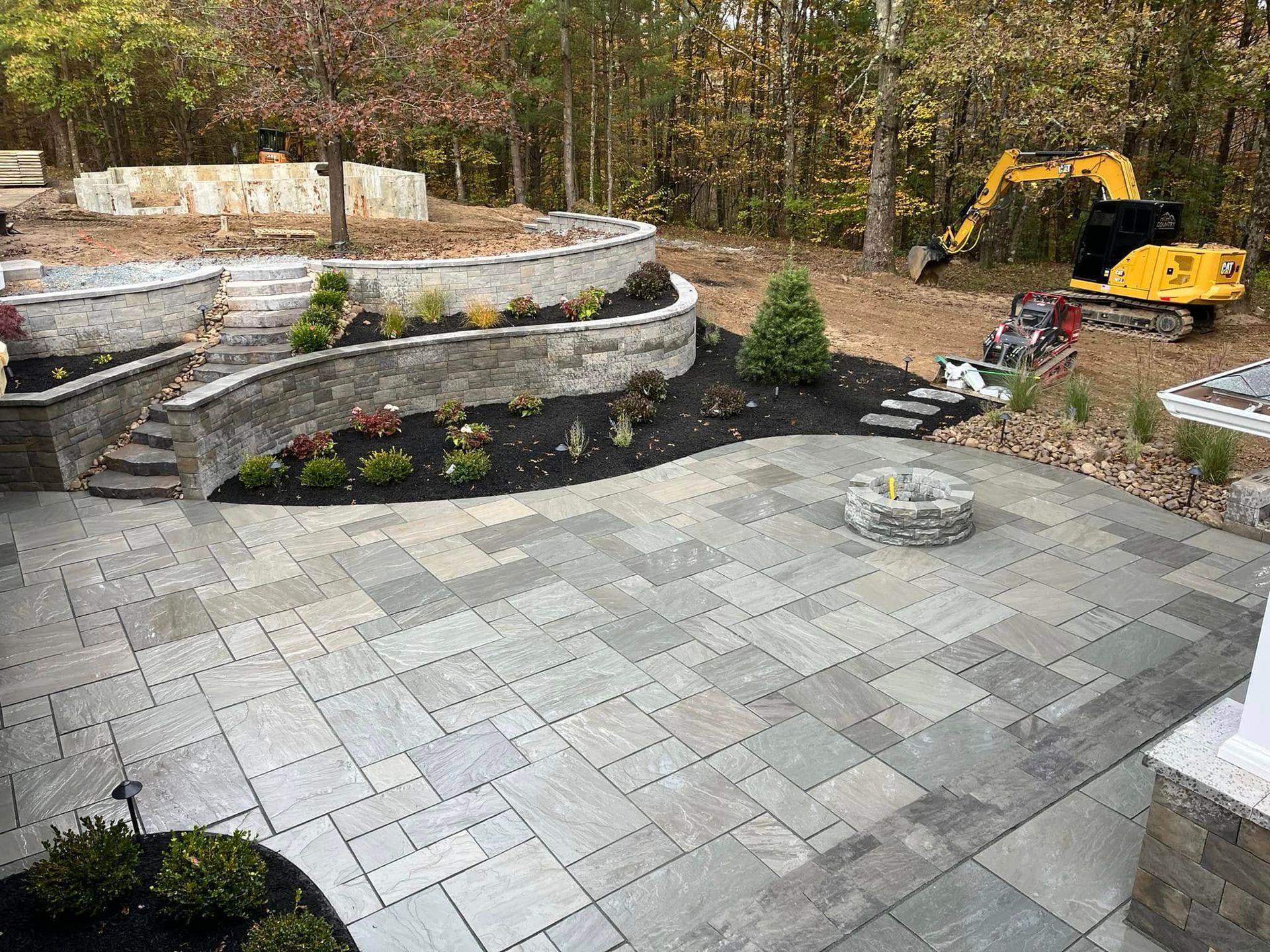 A large patio with a fire pit and a yellow excavator in the background.