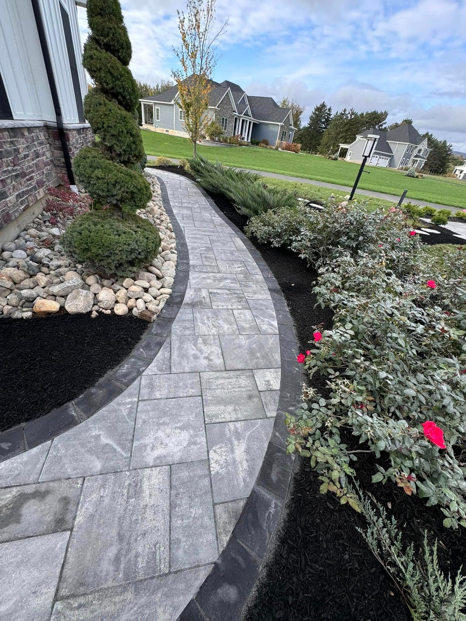 A brick walkway leading to a house with flowers and rocks.
