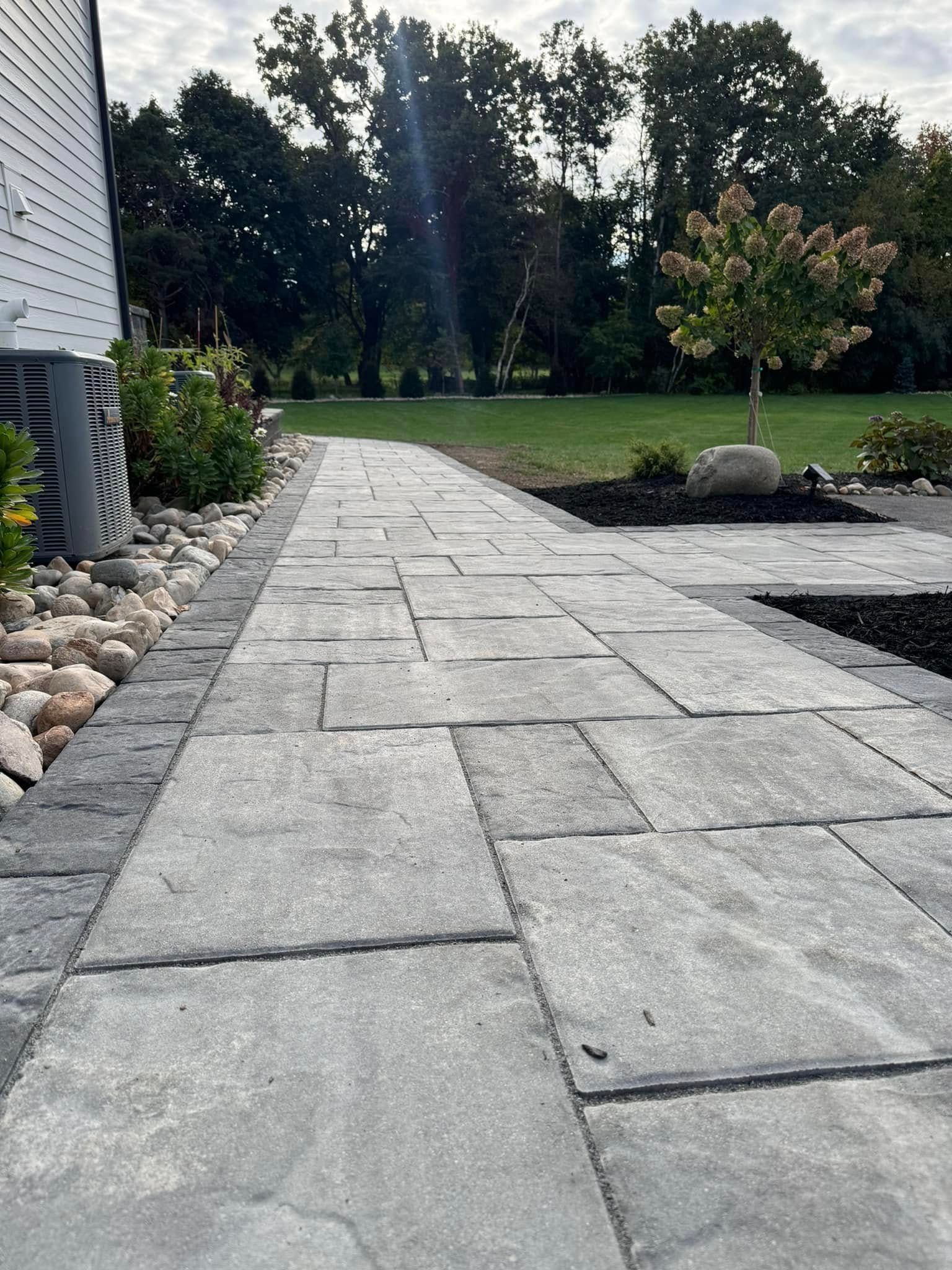 A stone walkway leading to a house with trees in the background.