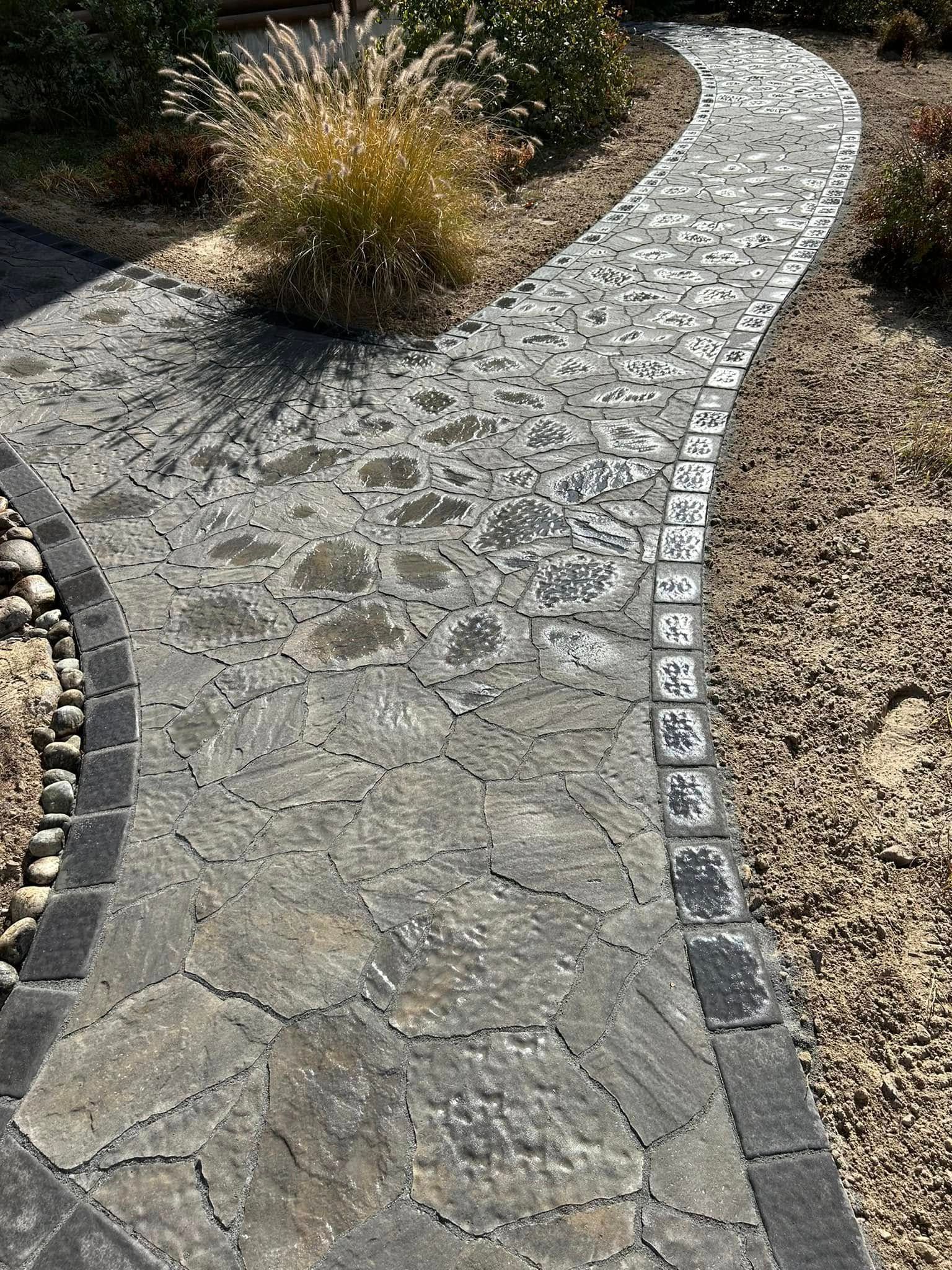 A stone walkway leading to a house in a garden.
