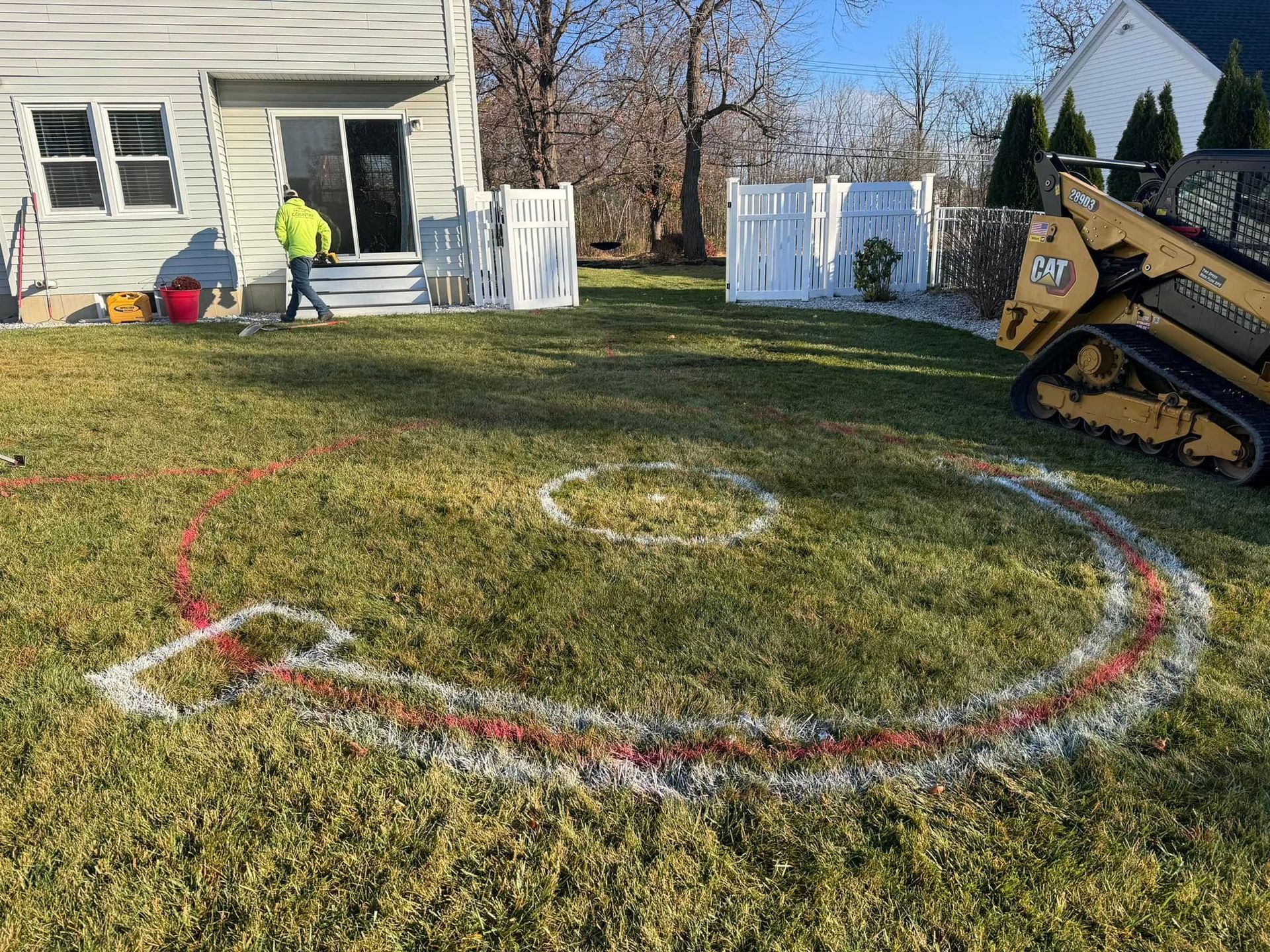 A man is standing in the grass in front of a house with a circle drawn in the grass.
