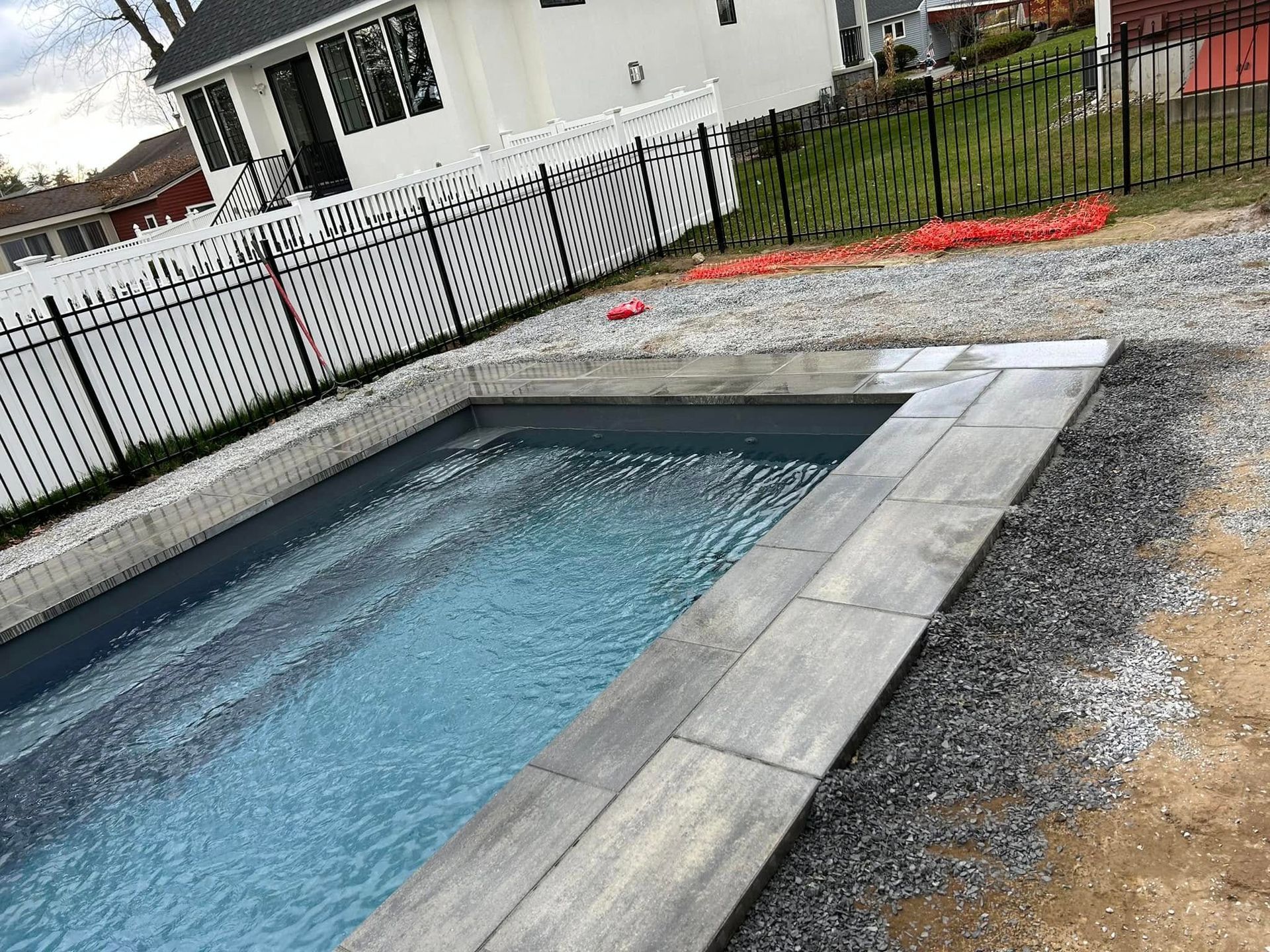 A large swimming pool surrounded by gravel and a fence in front of a house.