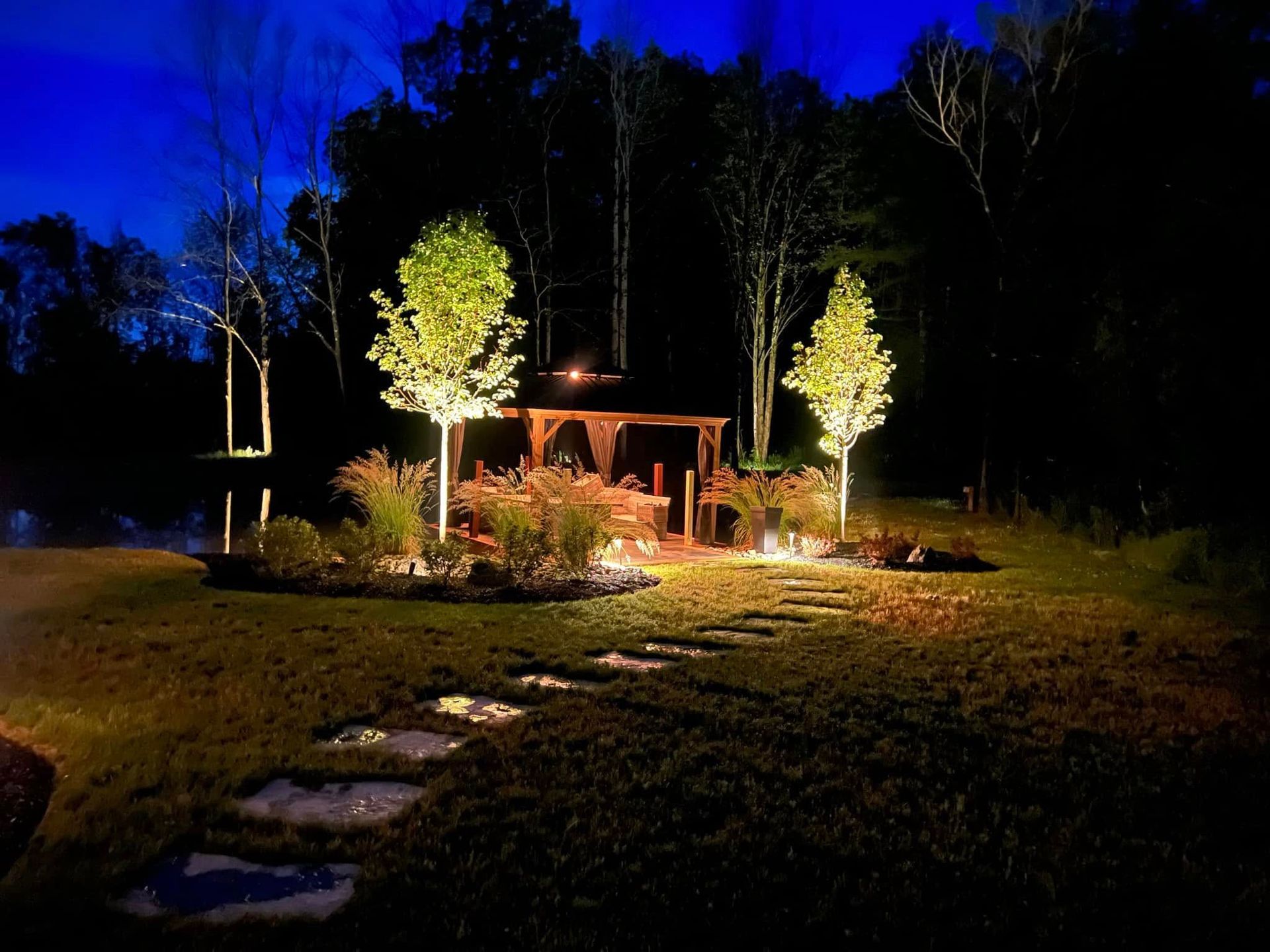 A gazebo is lit up at night in a backyard.