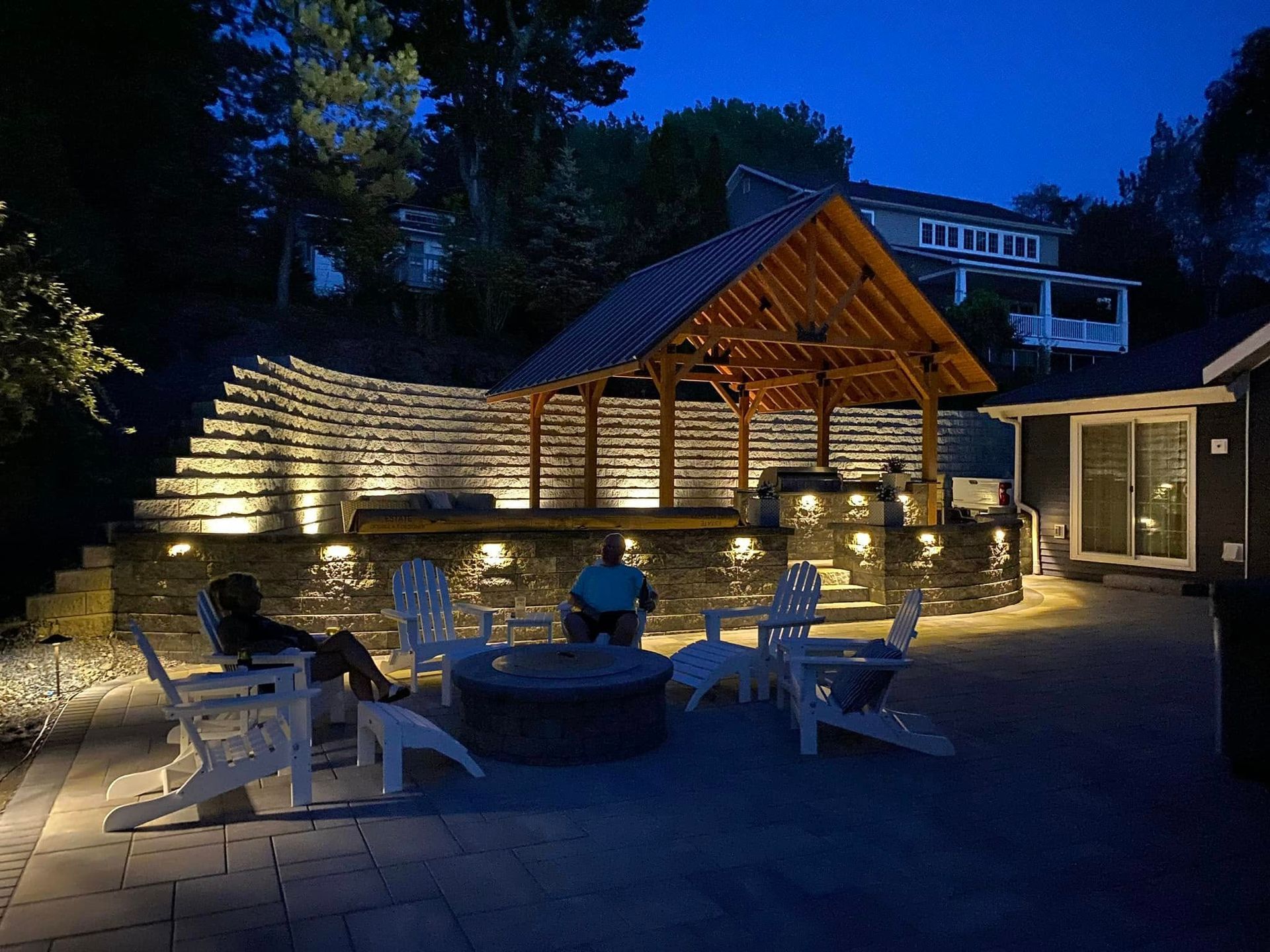 A man is sitting at a fire pit in a backyard at night.