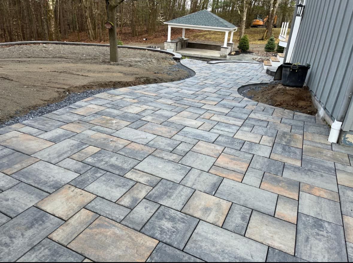 A brick walkway leading to a gazebo in a backyard.