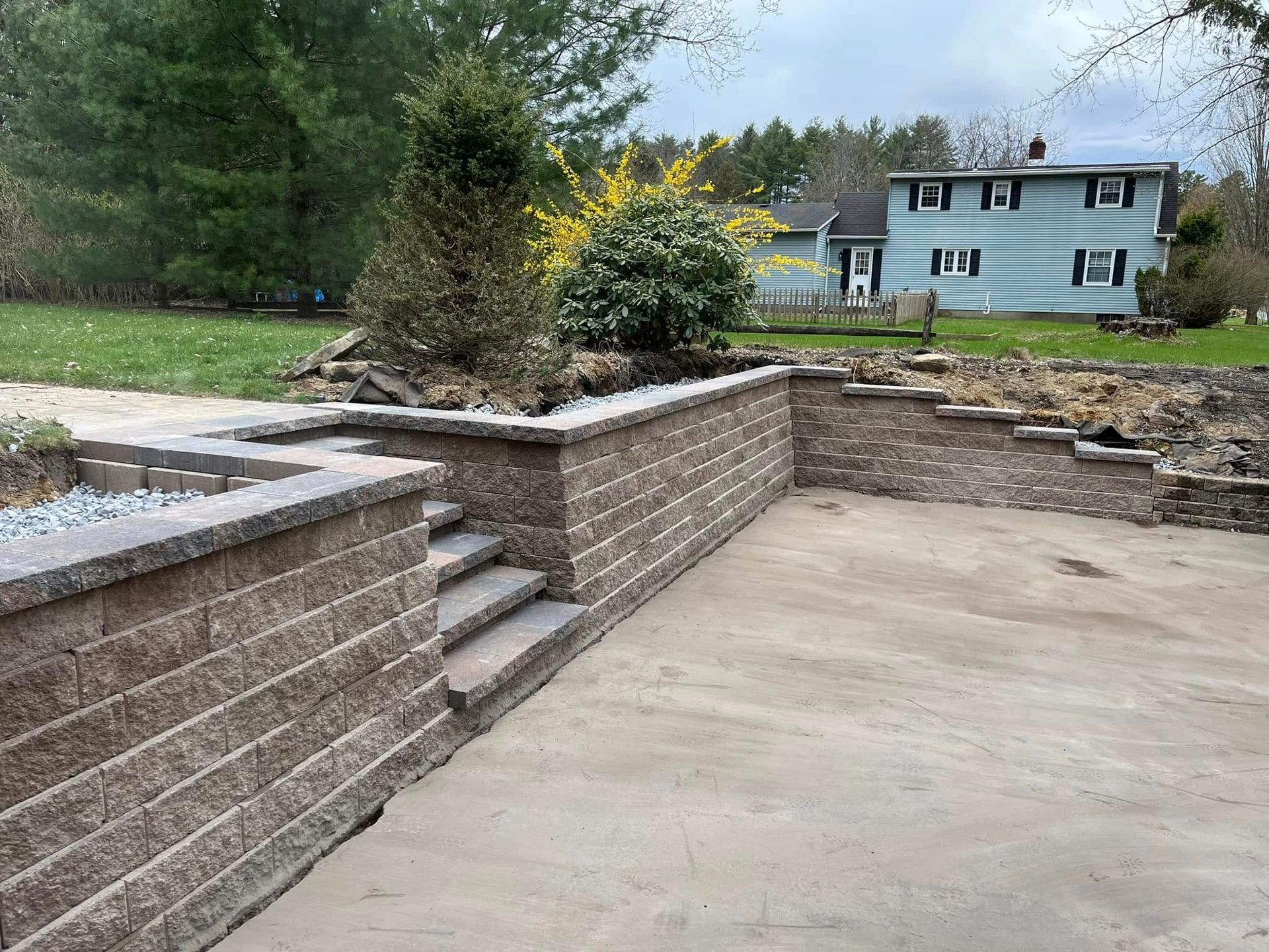 A brick wall with stairs leading up to it and a house in the background.