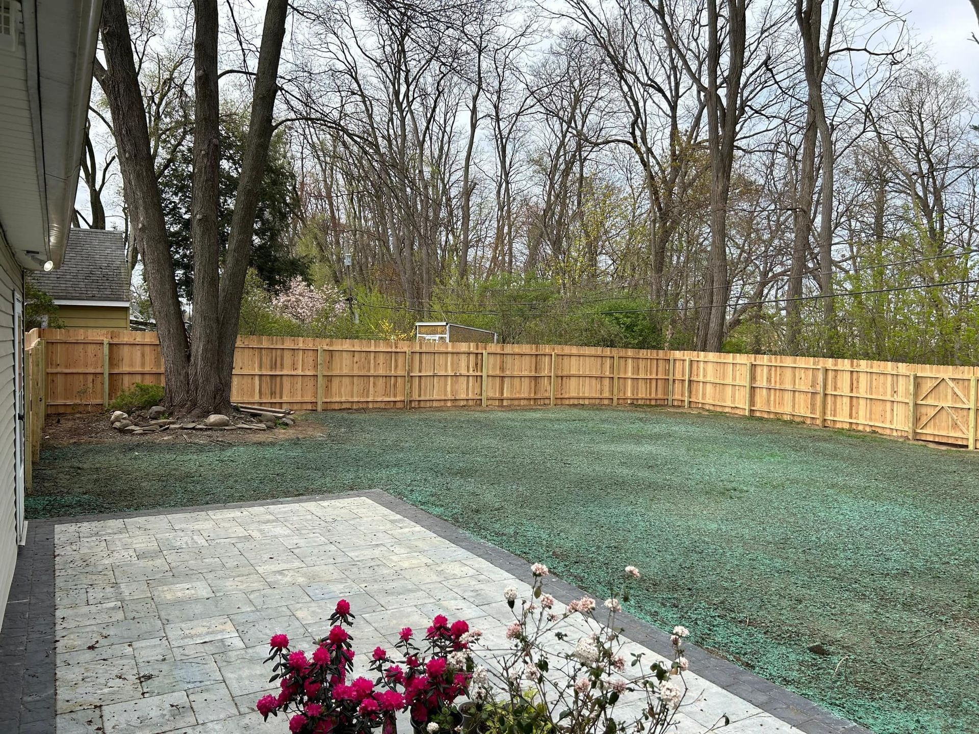 A backyard with a wooden fence and a patio with flowers in the foreground.