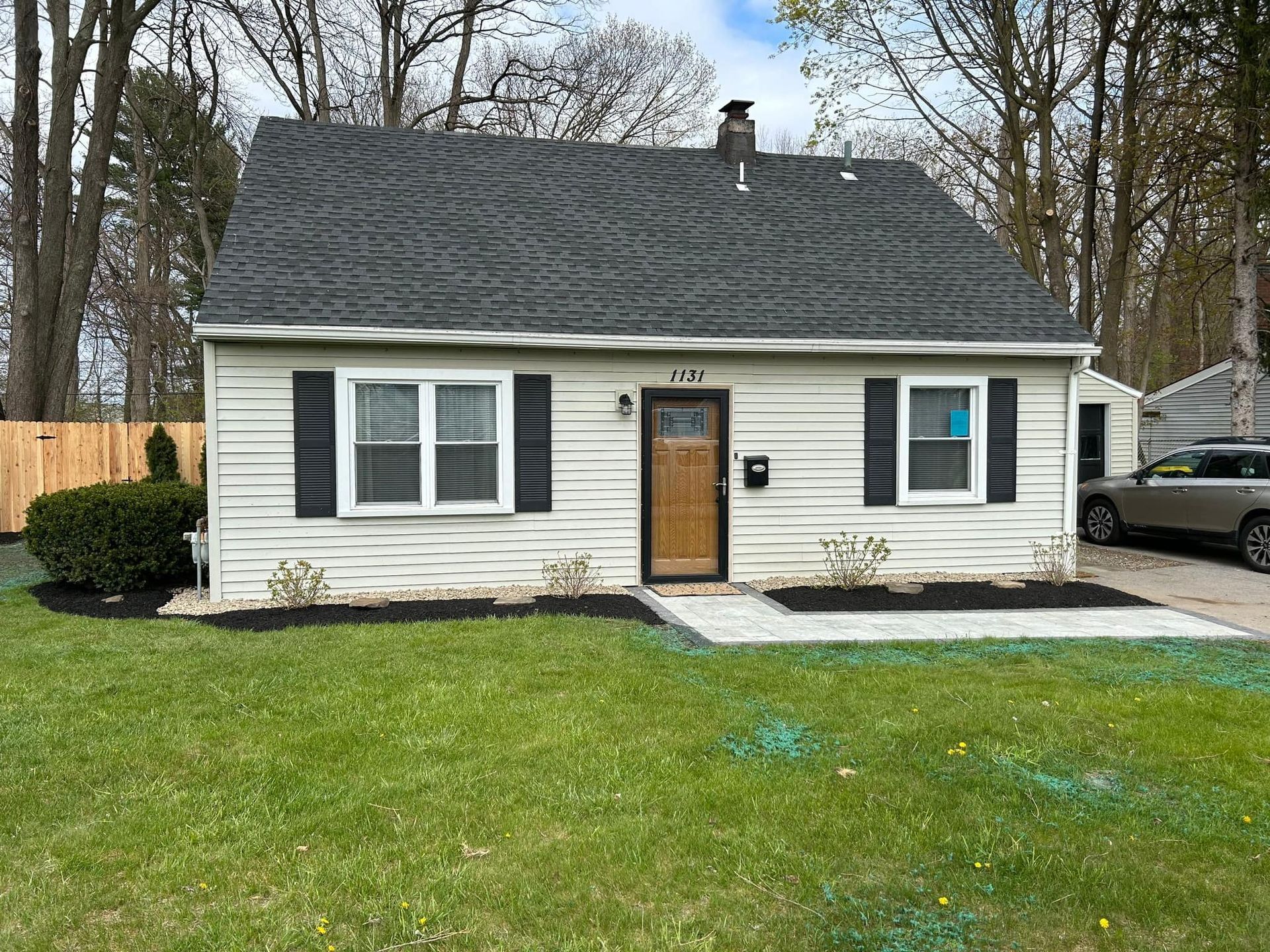 A small white house with black shutters and a car parked in front of it.